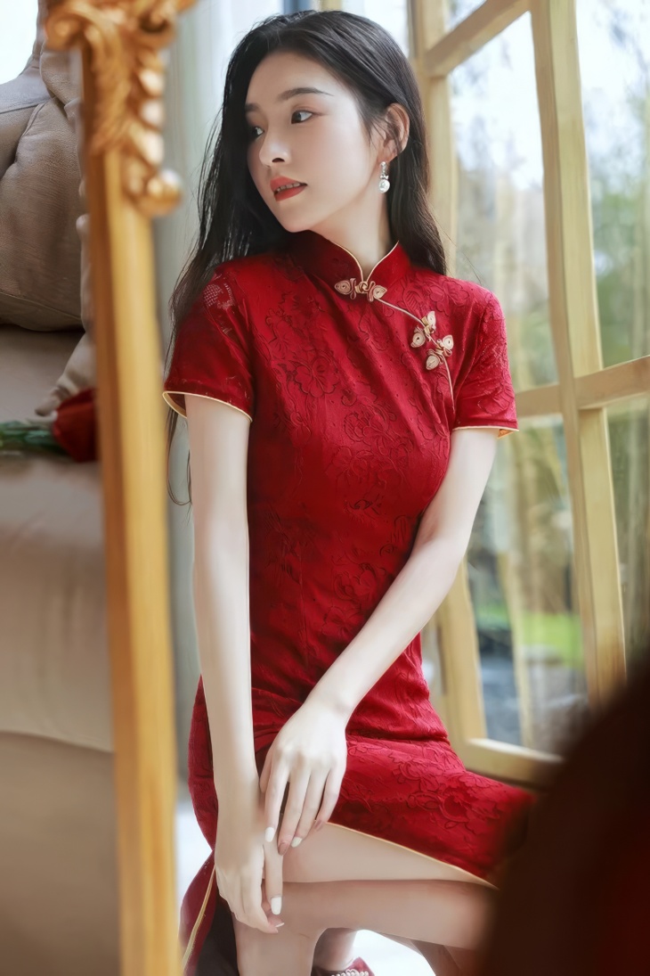 Qipao largo rojo burdeos de encaje con cuello mandarin y mangas cortas, vista lateral sentada junto a ventana